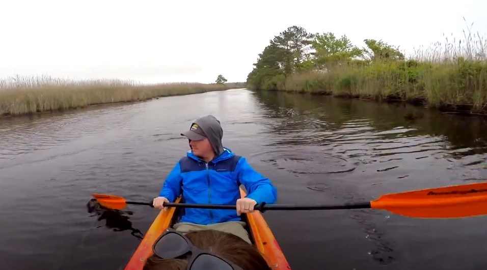 A man paddles a kayak down a flowing river surrounded by lush greenery