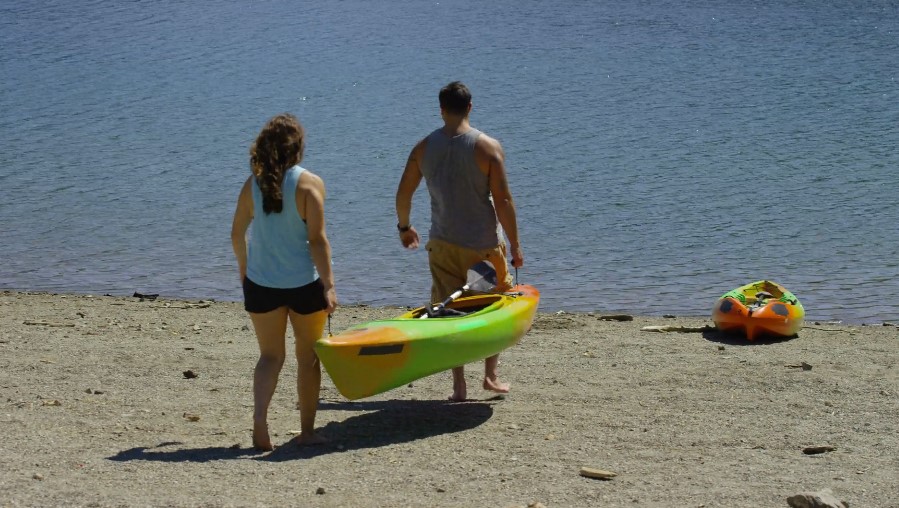 A man and woman walk along the beach, pulling kayak beside them on the sandy shore