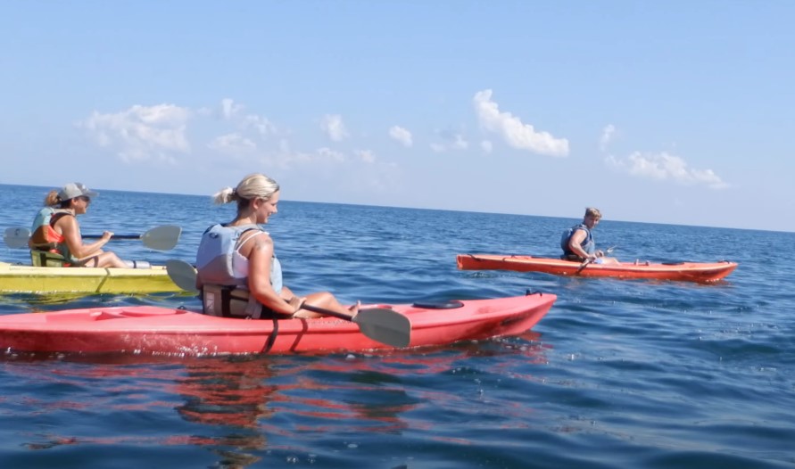 Three individuals paddling in colorful kayaks on a calm ocean under a clear blue sky