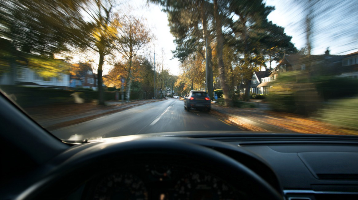 View from inside a moving car driving down a suburban street with blurred scenery
