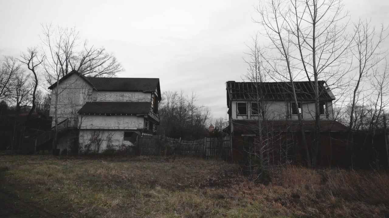 Two decaying wooden buildings with overgrown grass and leafless trees, set against a gray sky at an abandoned Renaissance Faire
