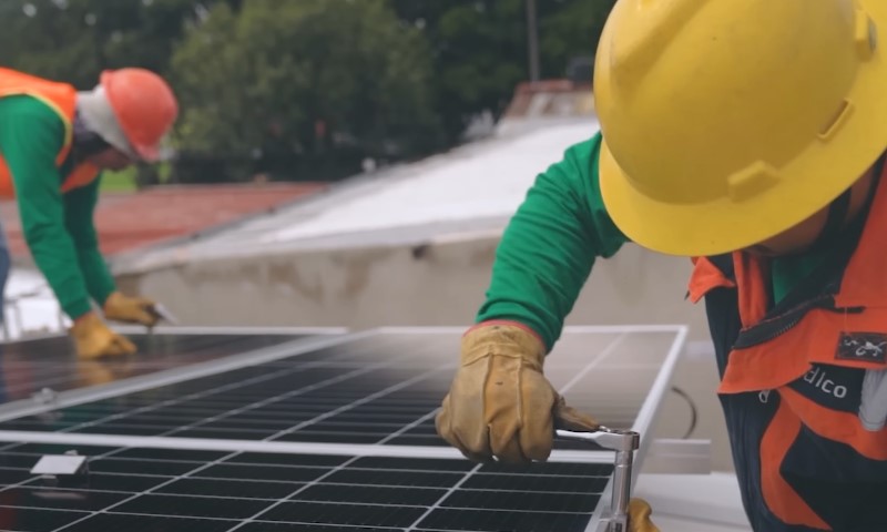 Two men in hard hats installing solar panels on a rooftop