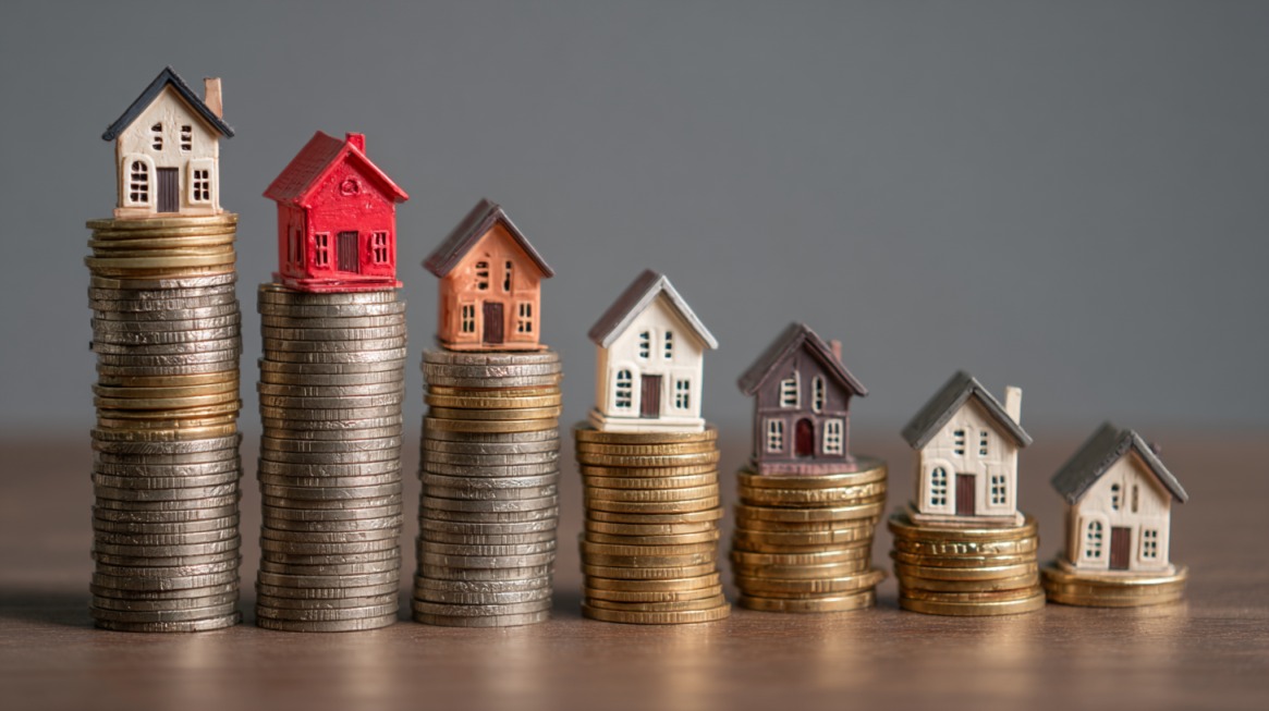 Small model houses placed on stacks of coins of varying heights, symbolizing fluctuating property prices