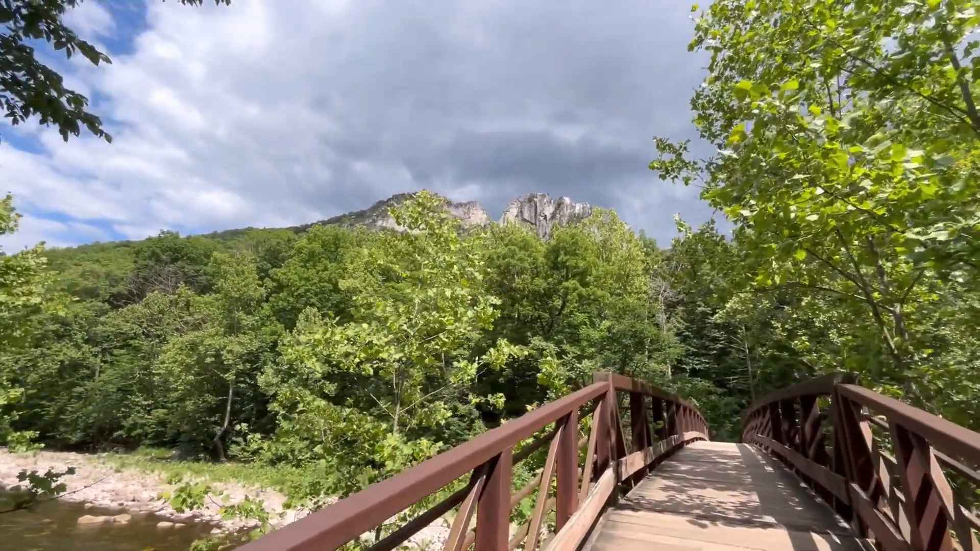 Wooden bridge surrounded by trees with Seneca Rocks rising in the background