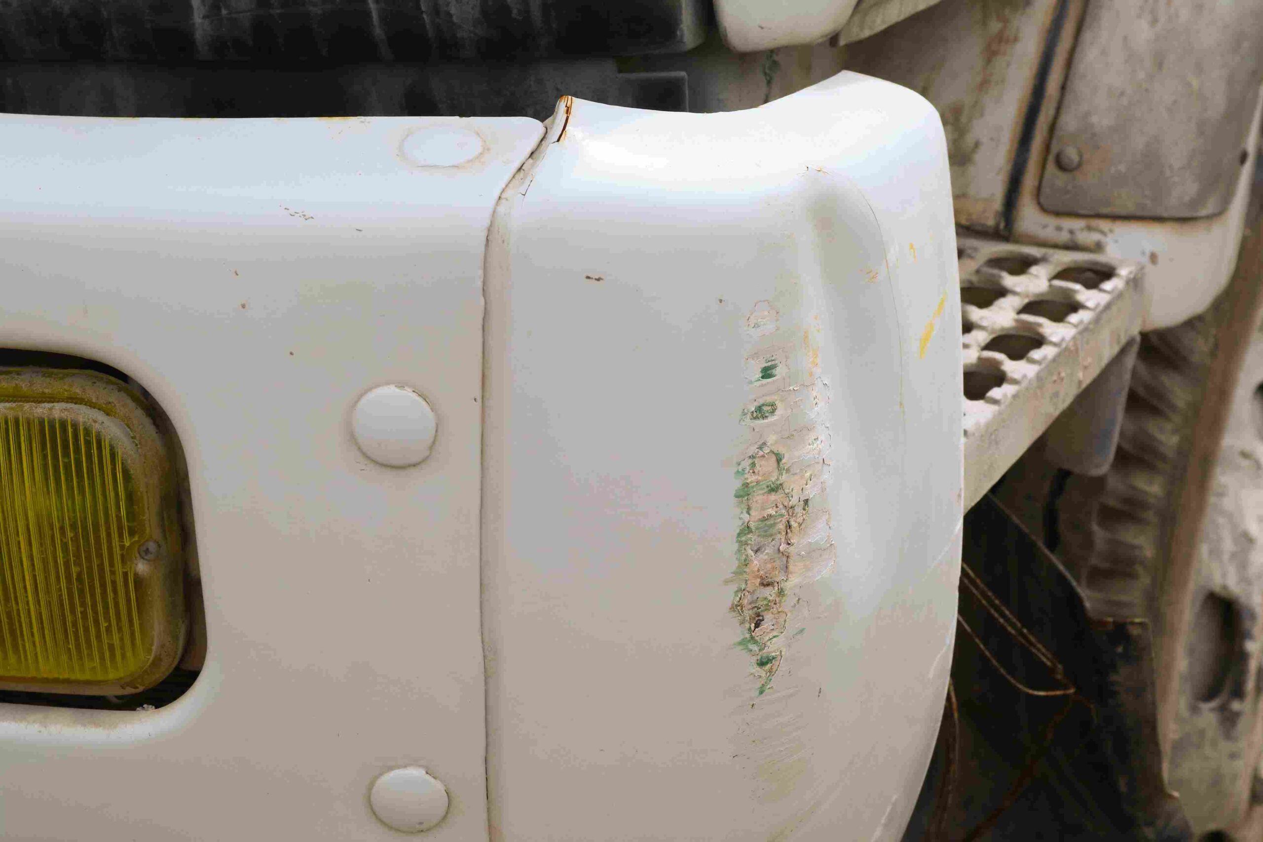 Close-up of a white vehicle bumper with scratches and scuff marks