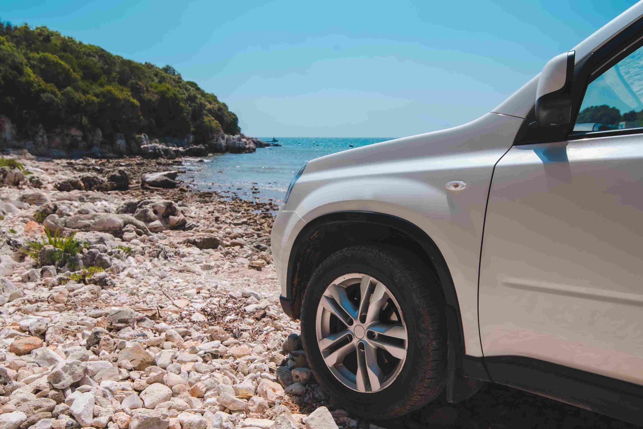 White SUV parked on a rocky beach near the ocean under a clear sky