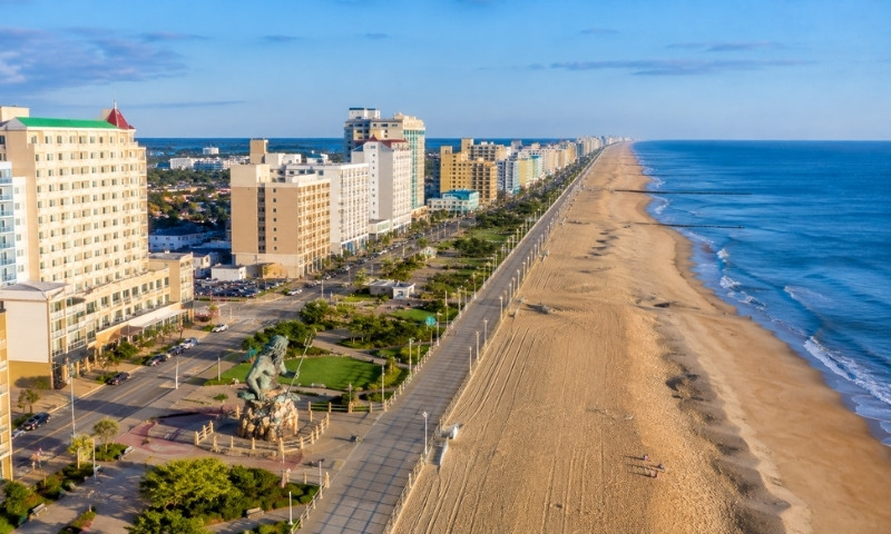 Aerial view of Virginia Beach with the oceanfront, sandy beach, boardwalk, hotels, and Neptune statue.